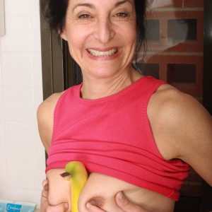 Older gal strips nude in the kitchen before taking a banana to her wooly gash